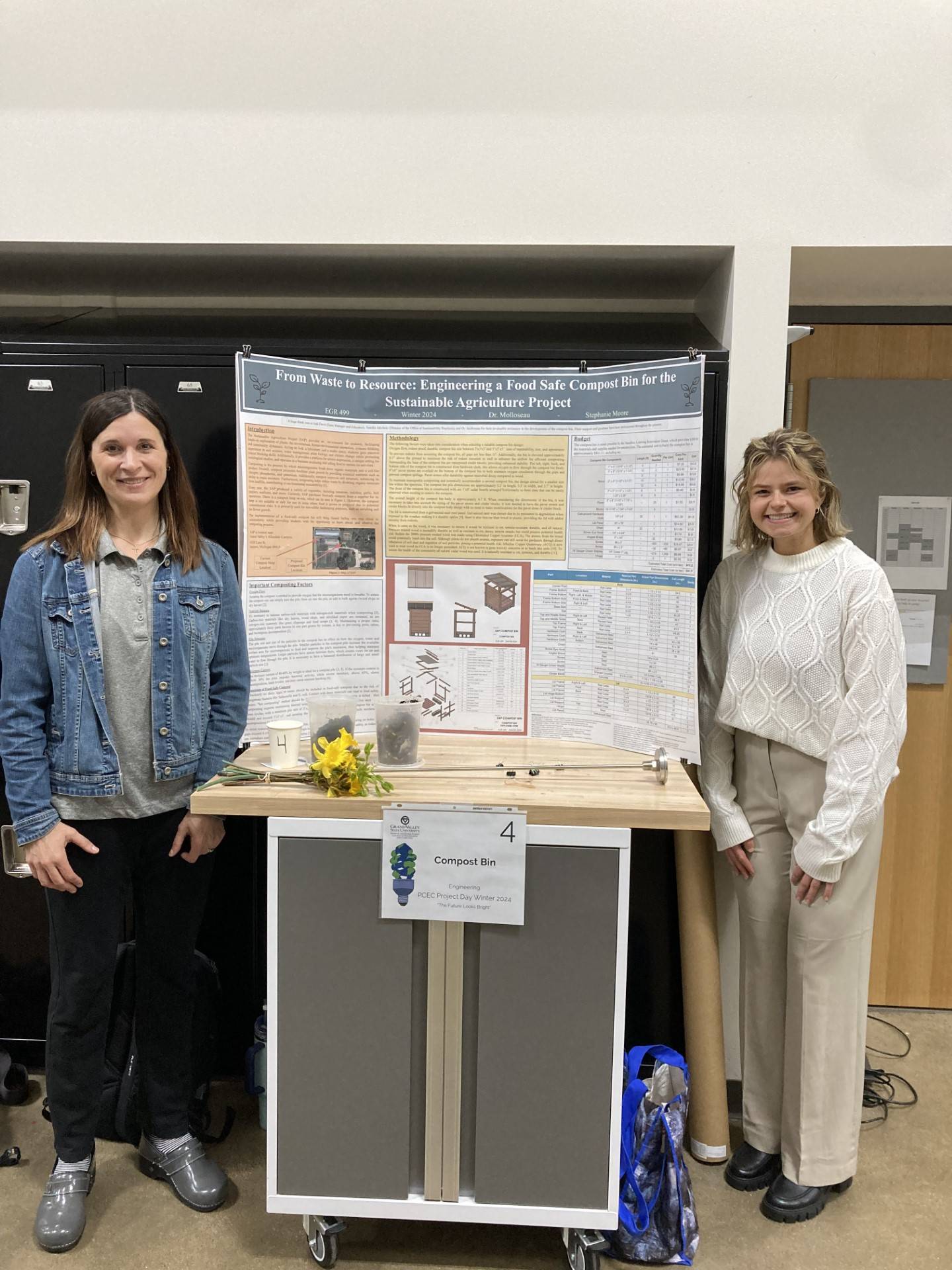 A picture of two people smiling and standing next to a poster